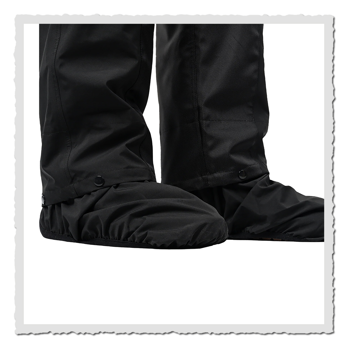 Nahaufnahme schwarzer Hosenbeinabschlüsse mit Stiefelschutz, Stofffalten und Druckknöpfe sichtbar.